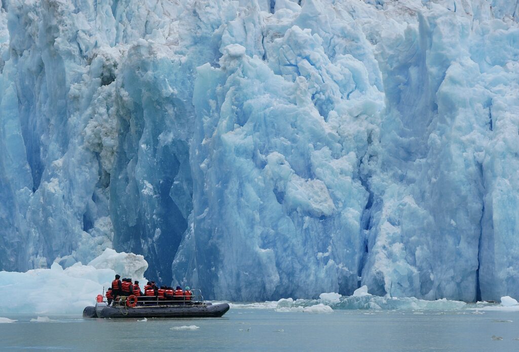 Zodiac full of travelers cruises past a glacier.