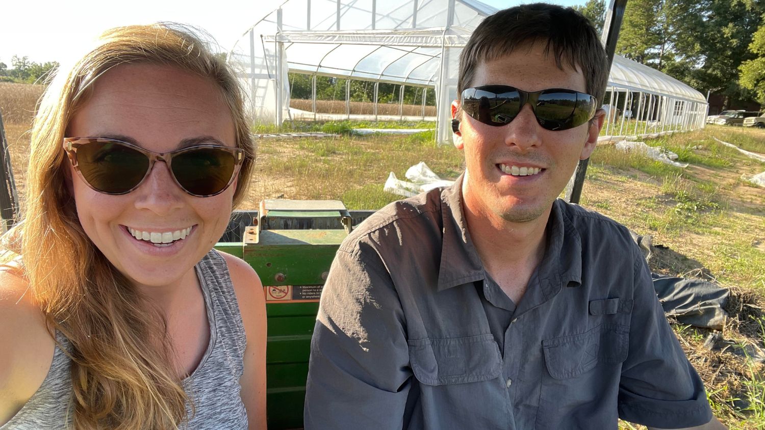 a couple taking a selfie wiht a greenhouse in the back