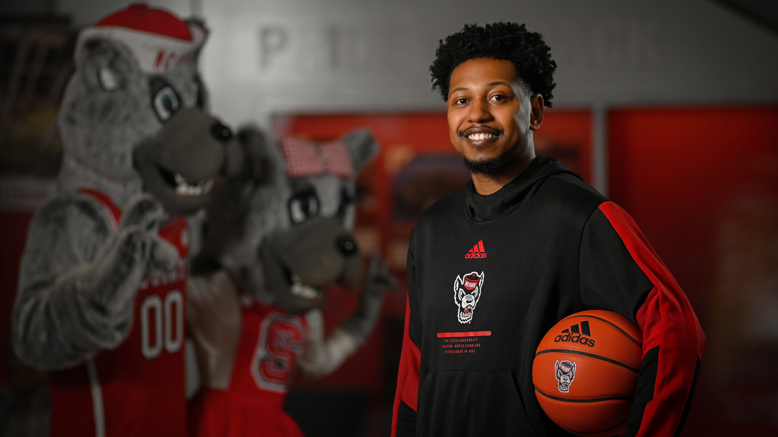 Jalen Latta holding a basketball with Mr and Ms Wuf in the background