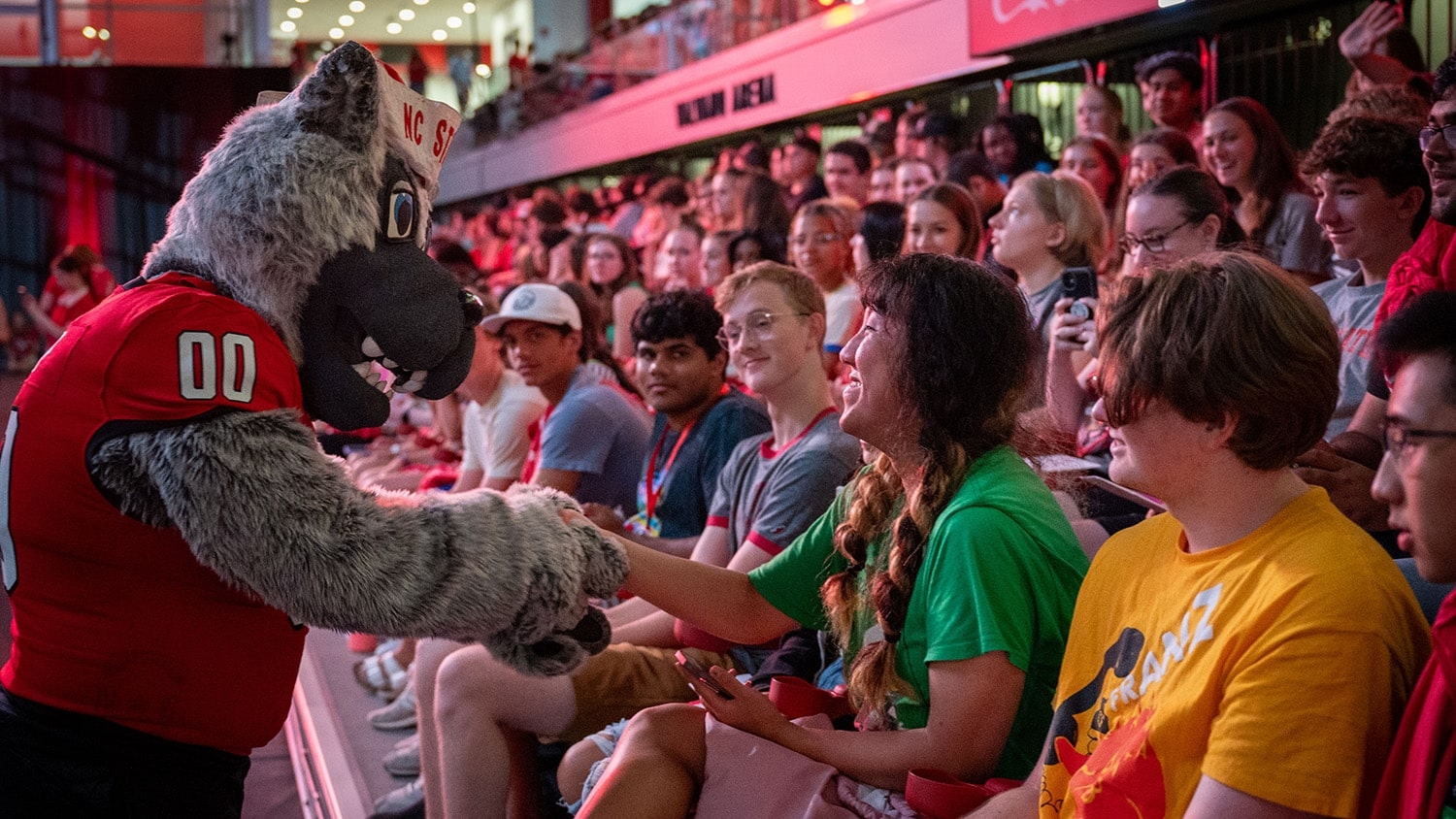 Mr. Wuf shakes hands with a new NC State student during Convocation in Reynolds Coliseum.