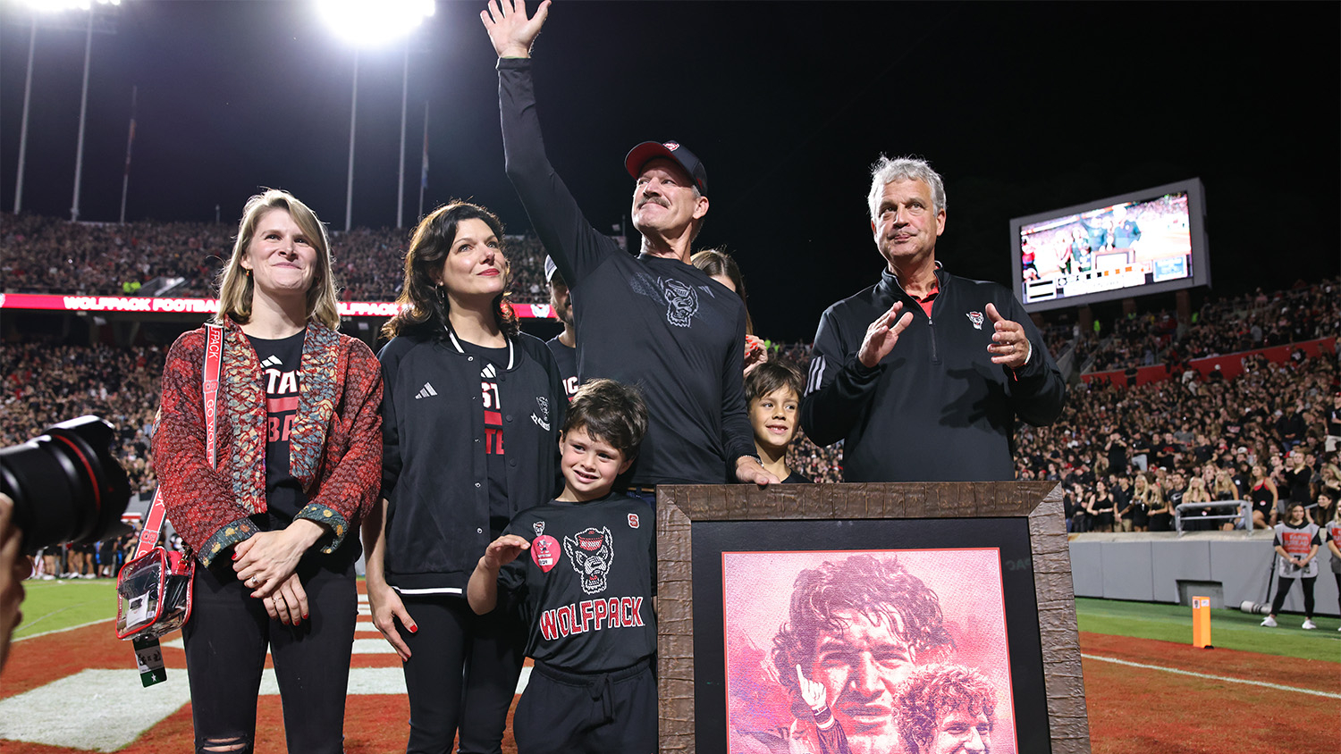 Bill Cowher on the field of Carter-Finley Stadium waves at the crowd along with his family and Athletics Director Boo Corrigan