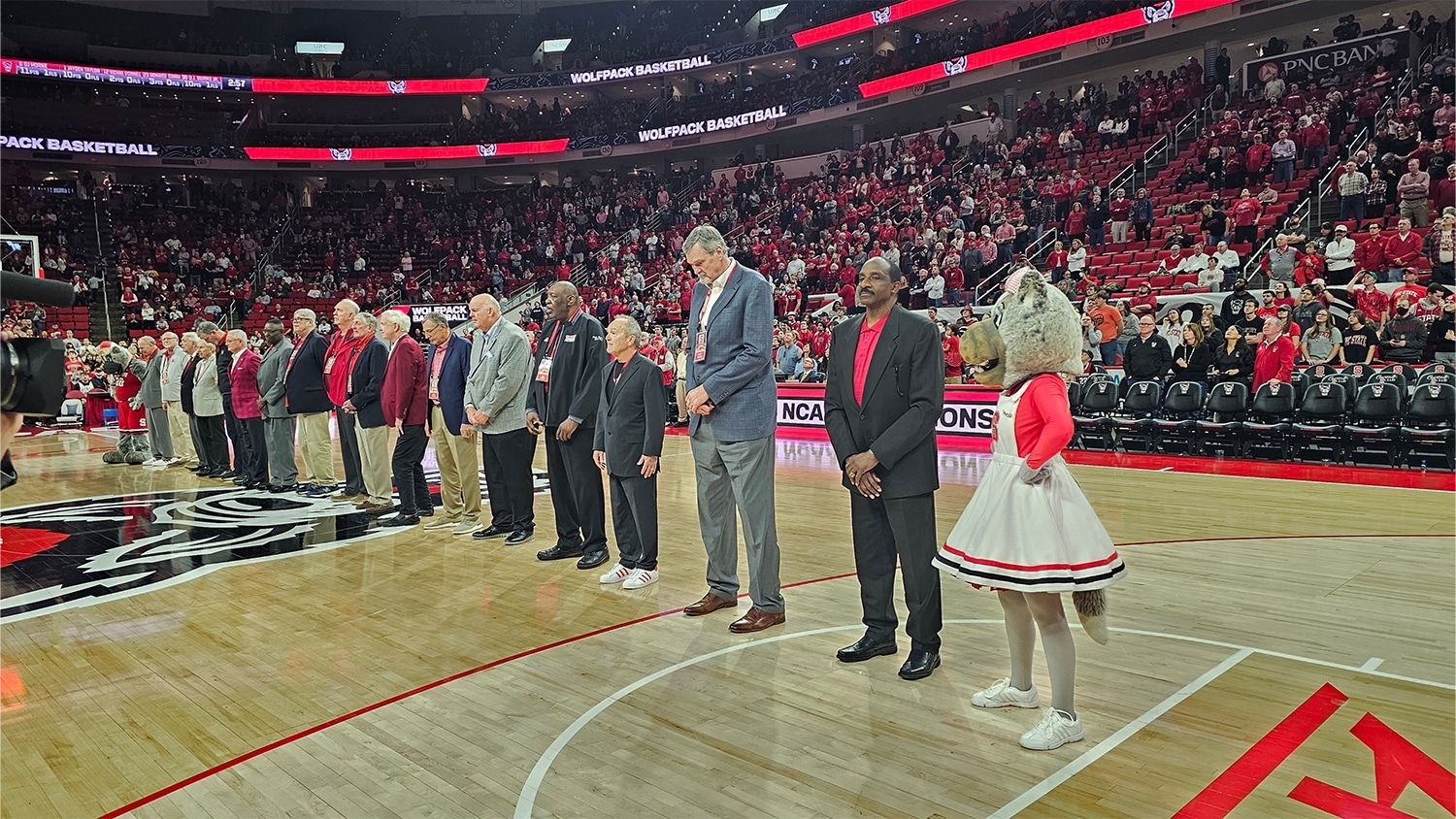 Members of NC State's 1974 NCAA Men's Basketball Championship team standing on the court of PNC Arena to be recognized for their accomplishment.