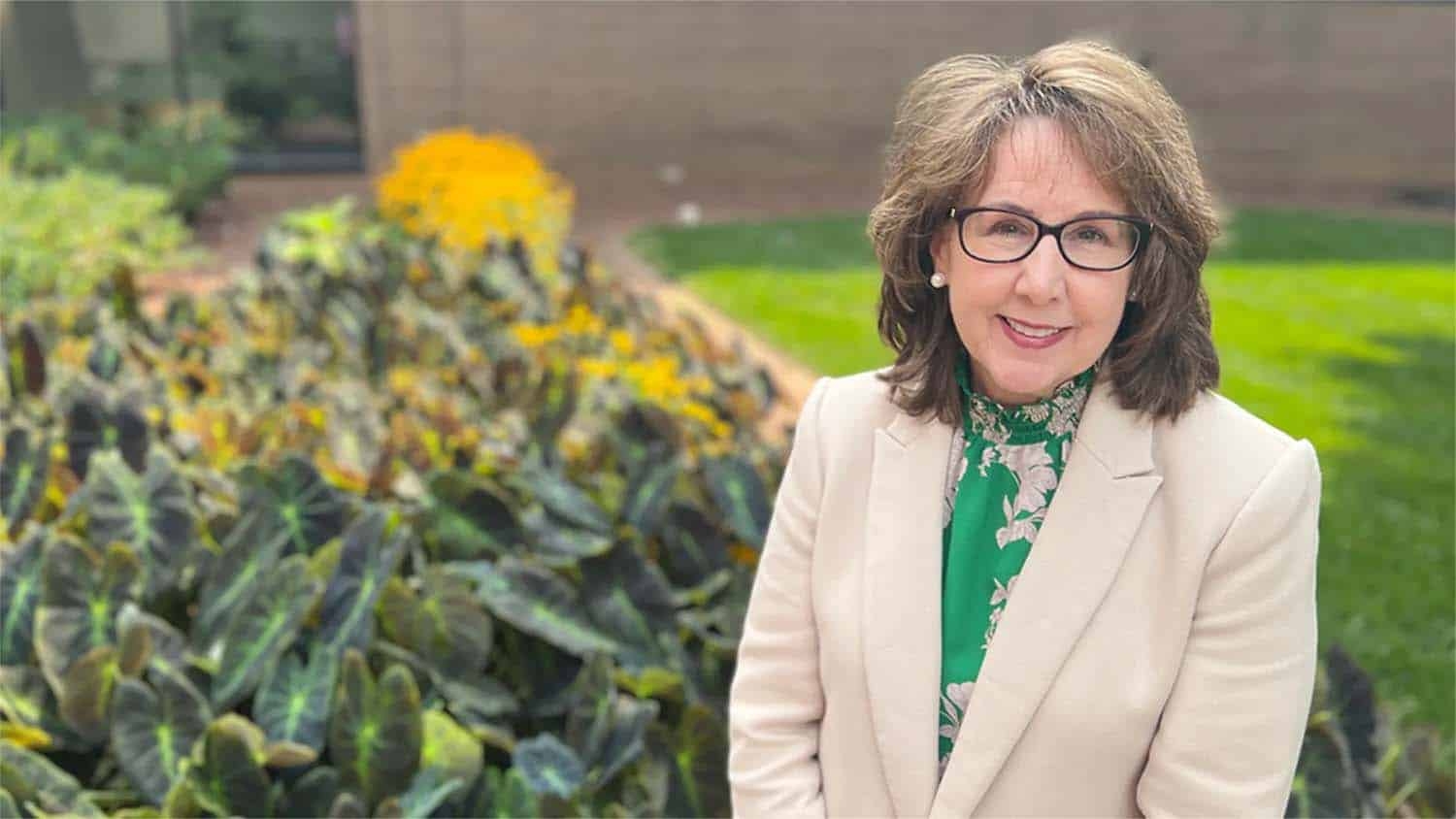 Leigh Brady sitting next to yellow blooming flowers on a grassy lawn