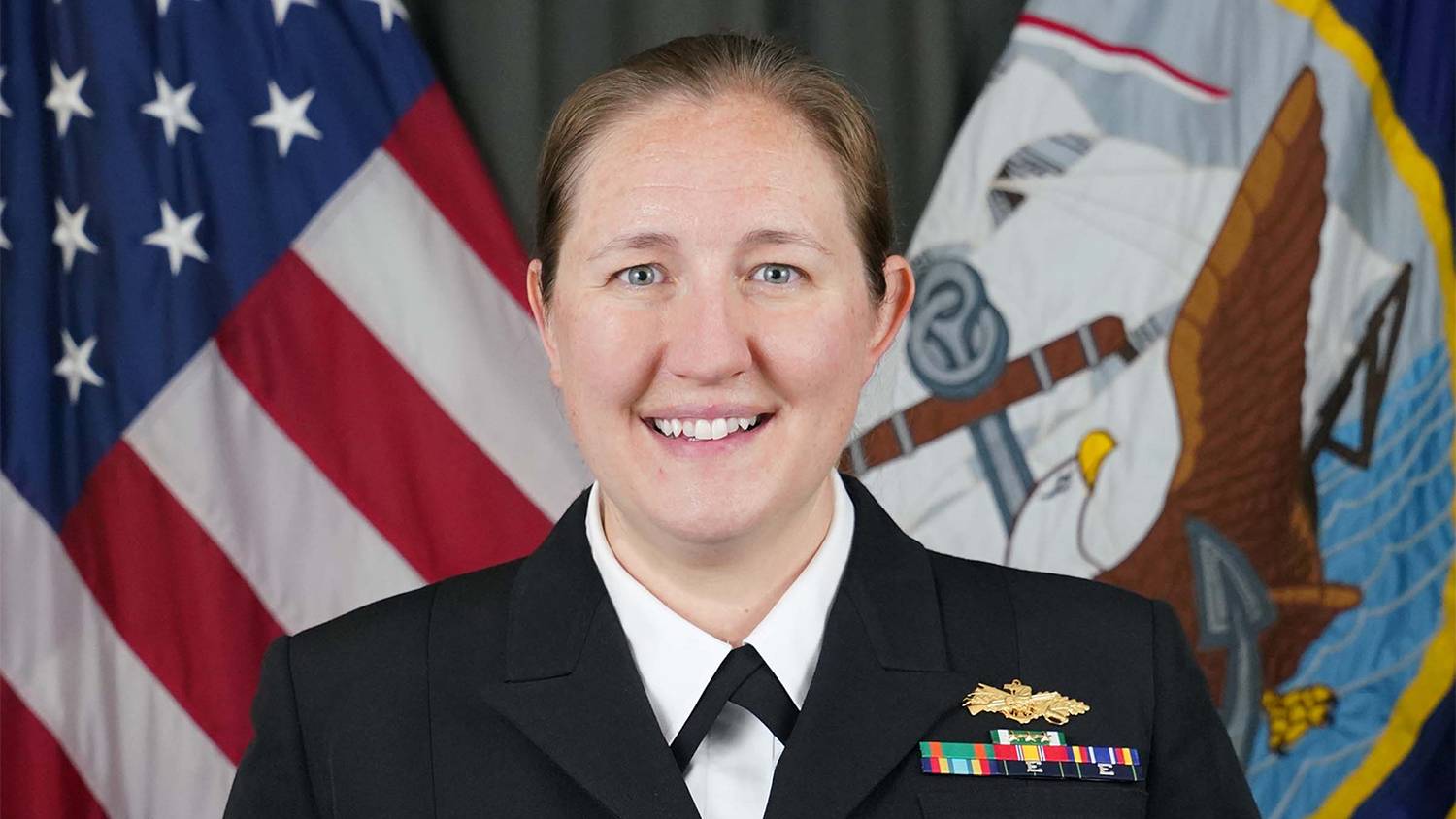 Genevieve Flatgard poses for a portrait while wearing her military uniform. The United States flag, left, and the United States Navy flag, right, are behind her.