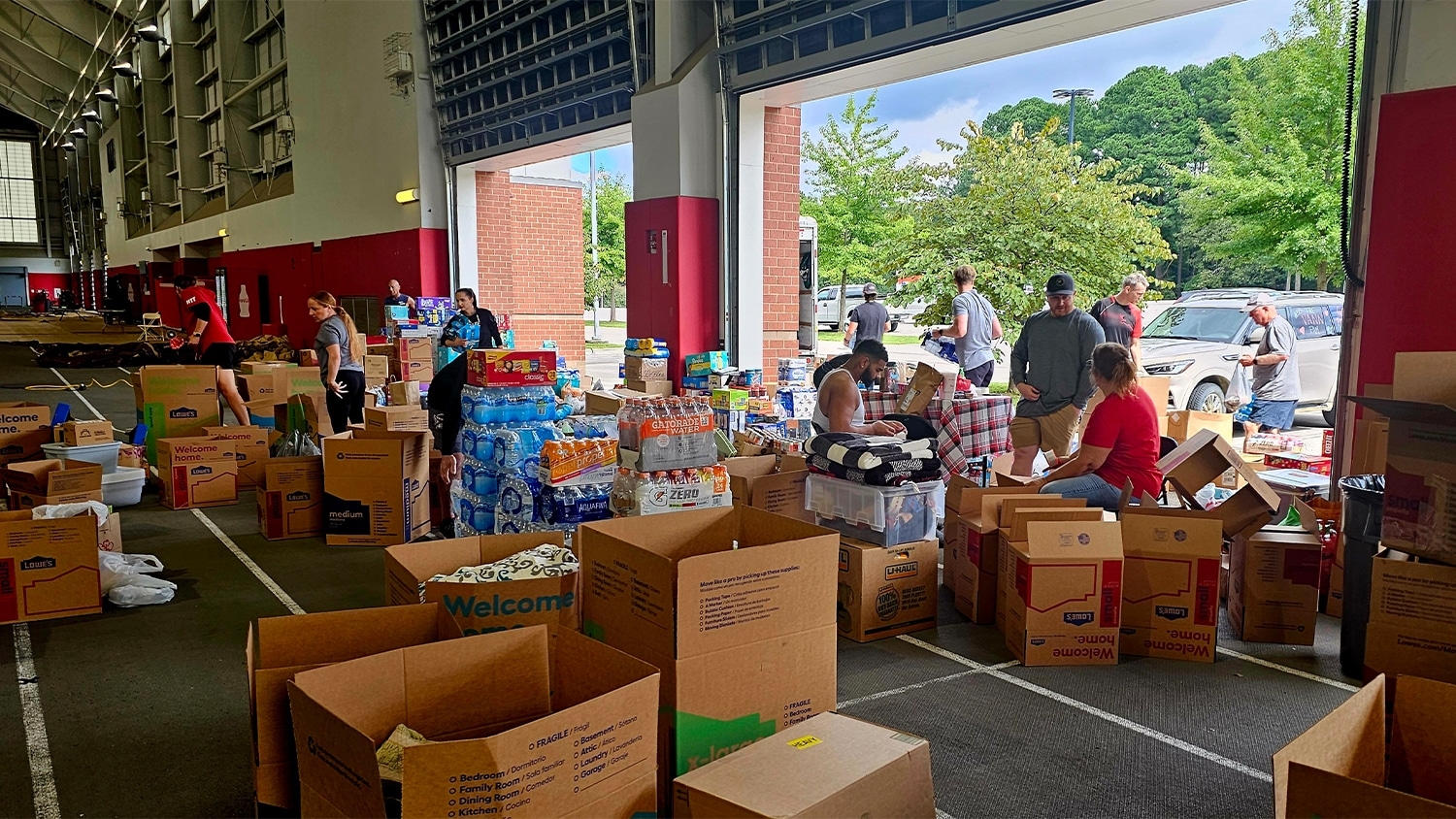 Staff and community members load boxes of supplies at the NC State football team's practice facility