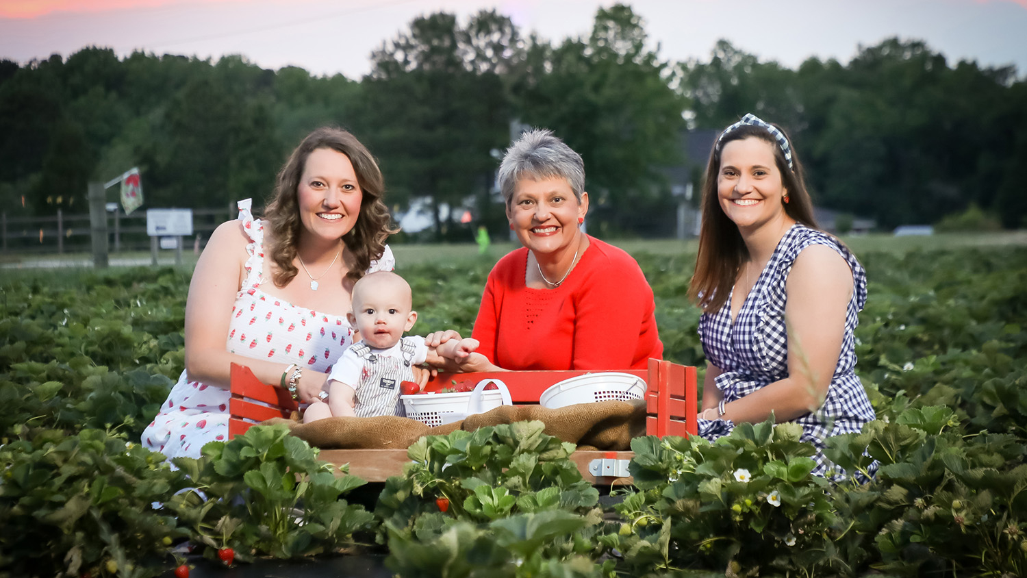 Three women and baby sitting in a strawberry field smiling