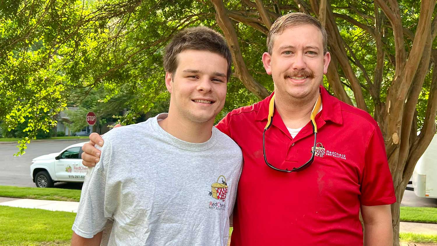 Two family members working for RedCheck Pest Solutions pose along a sunny suburban street.